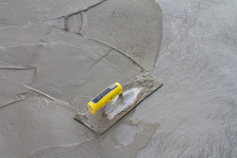 Close up of a trowel smoothing wet concrete surface during finishing work for a durable floor or patio base.