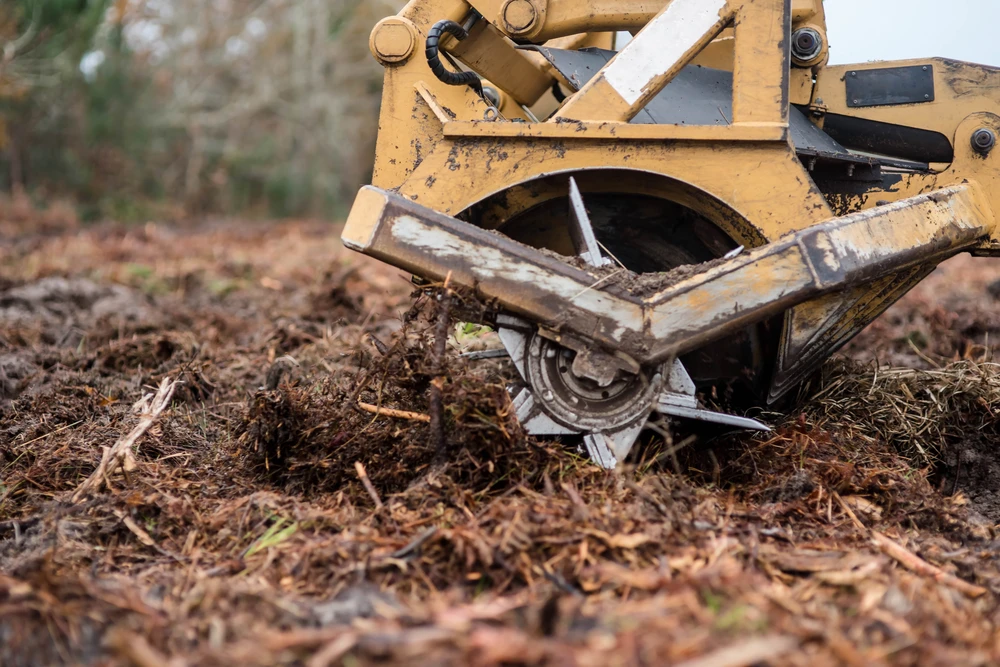 Close up of a demolition machine grinding and tearing through soil and debris during a site clearing project.