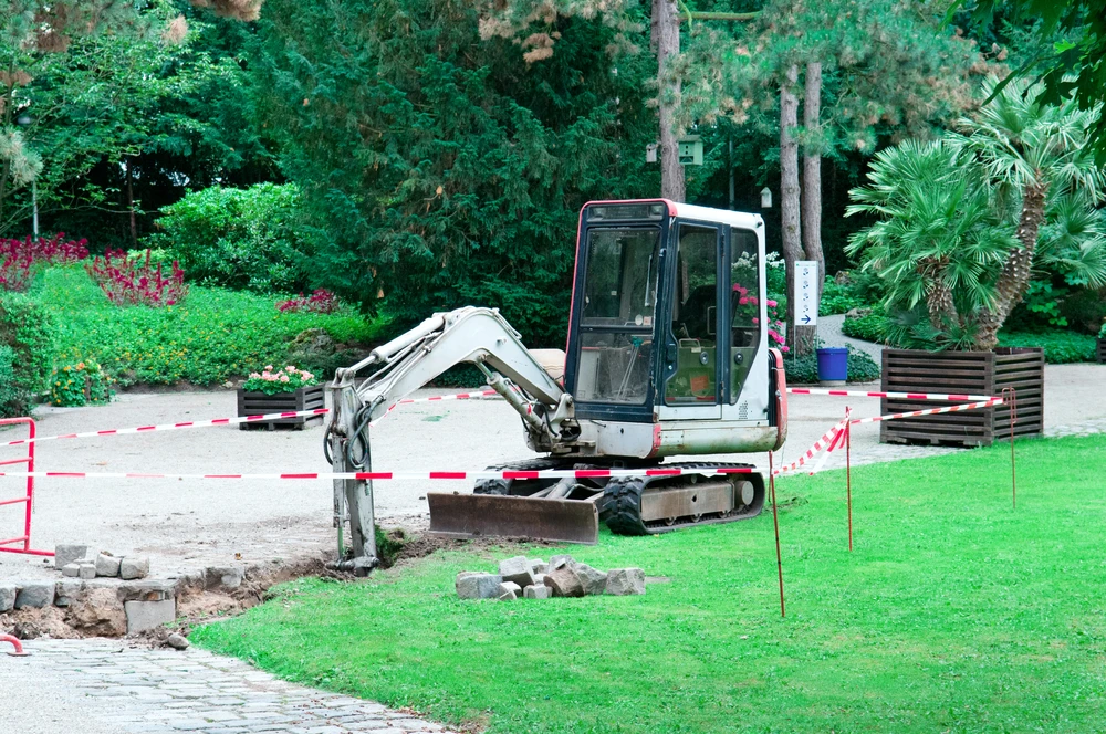 Compact excavator parked in a landscaped park area during a small scale demolition and ground removal project.