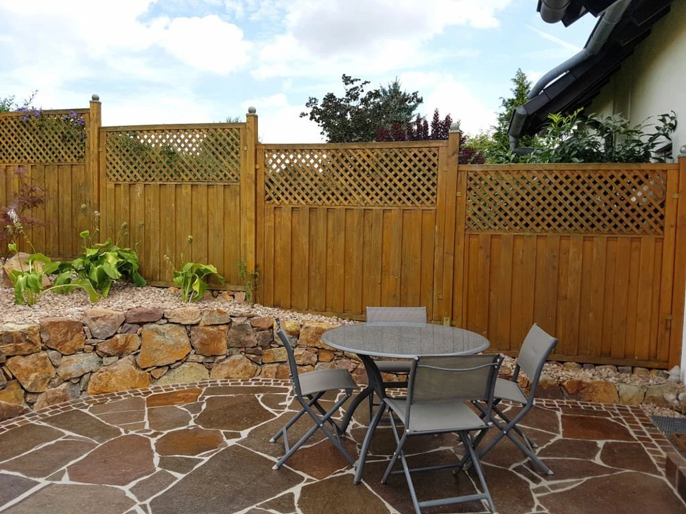 Custom wooden privacy fence with lattice top enclosing a backyard patio and stone retaining wall in Potomac MD.