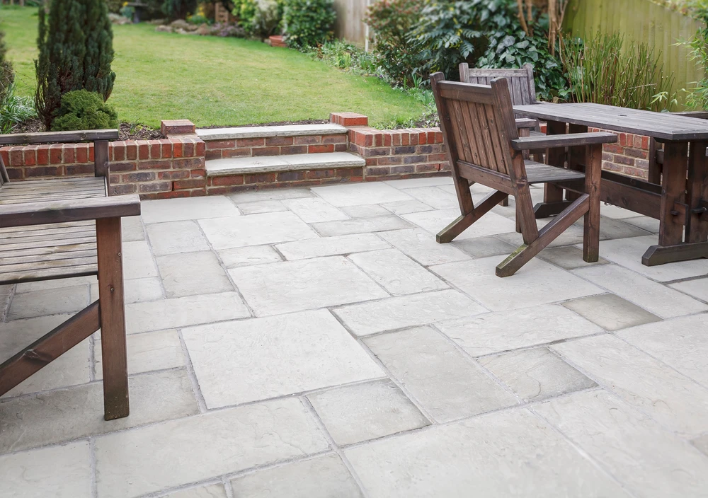 Stone patio with wooden dining furniture, brick steps, and raised borders demonstrating classic residential hardscaping.