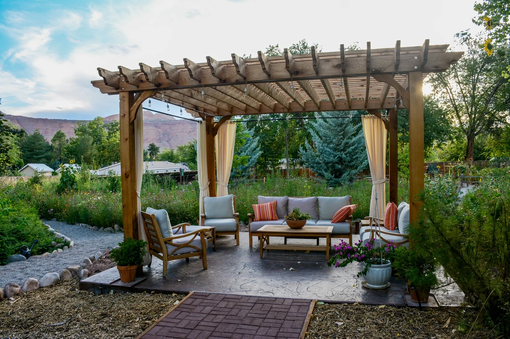 Wood pergola with cushioned outdoor seating and curtains set in a garden with mountain views, creating a relaxed Potomac MD style retreat.