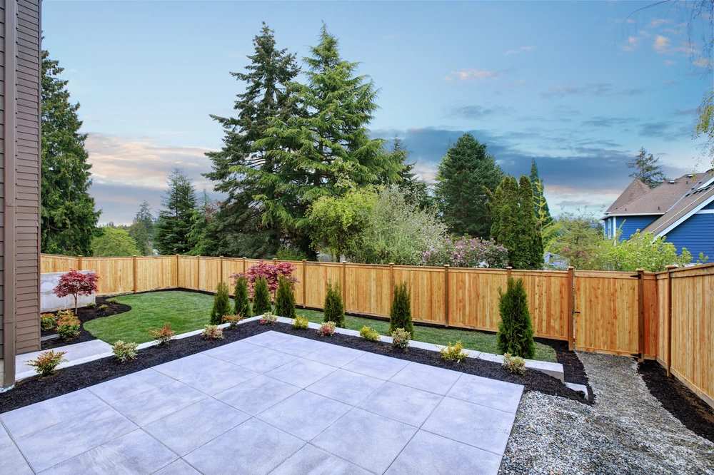 New stone patio and landscaped lawn bordered by a custom wood privacy fence and evergreen trees in a Bethesda MD residential yard.
