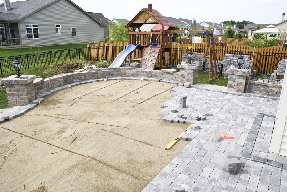 Backyard patio under construction with compacted sand base for long-lasting stability.