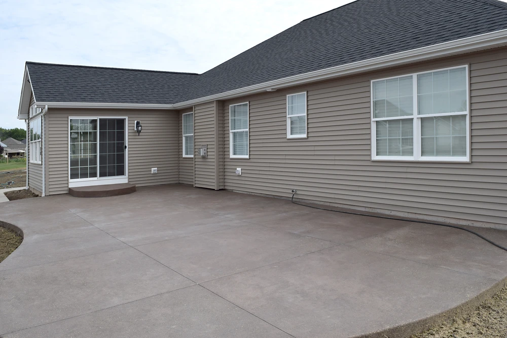 Smooth concrete patio wraps around a beige home with sliding glass doors and white trimmed windows.
