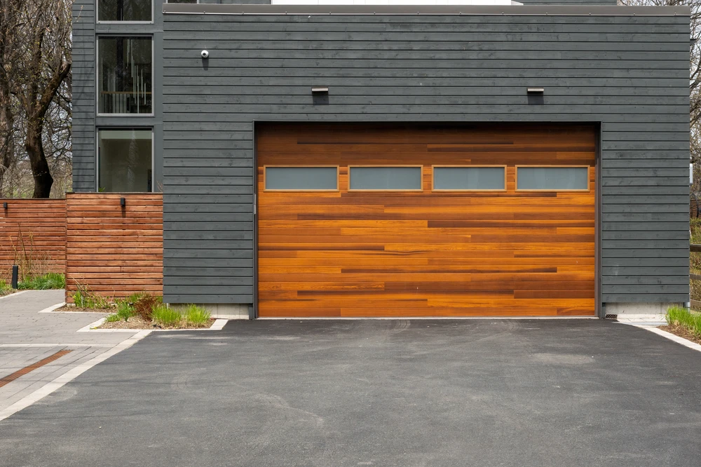 Evergreen Enterprises service area 1 - Evergreen Enterprises Curved blacktop driveway leading to a large stone and siding home with two white garage doors and landscaped lawn.
